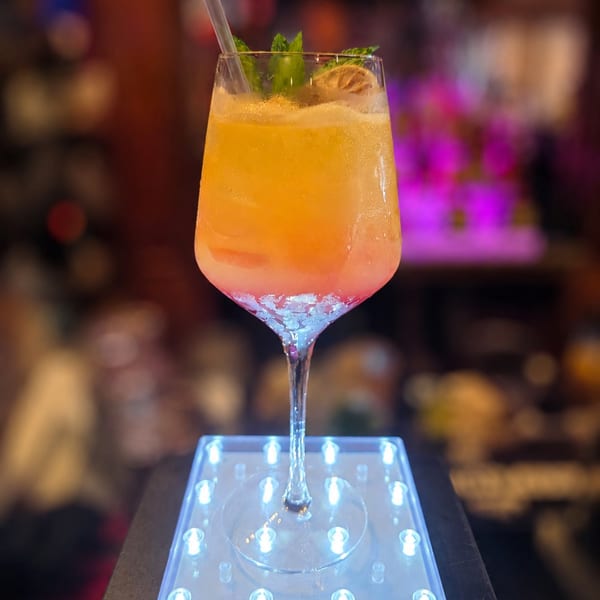 Colorful cocktail with mint and lime sits on a light-up coaster in a bar setting.