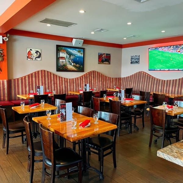 Empty dining room at Sangria Cafe with wooden tables, red striped booths, and a large TV showing soccer.