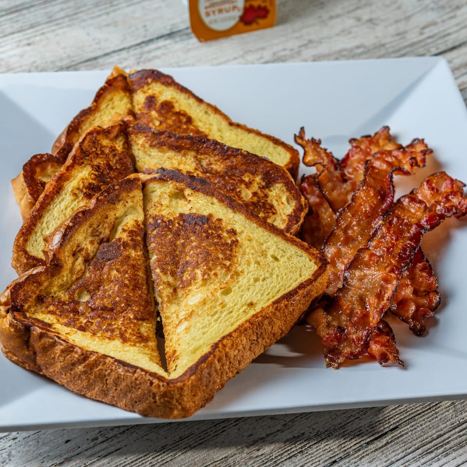 Golden brown French toast slices and crispy bacon strips on a white rectangular plate.