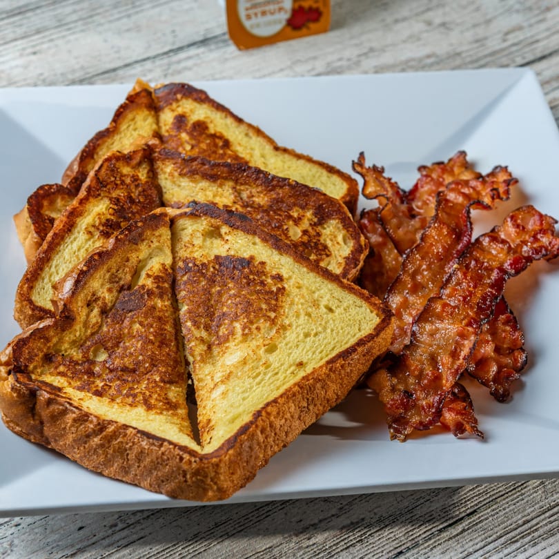 Golden brown French toast slices and crispy bacon strips on a white rectangular plate.