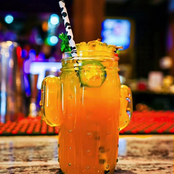 Orange drink in a cactus glass with pineapple, jalapeño, and a cow-print straw on a bar.