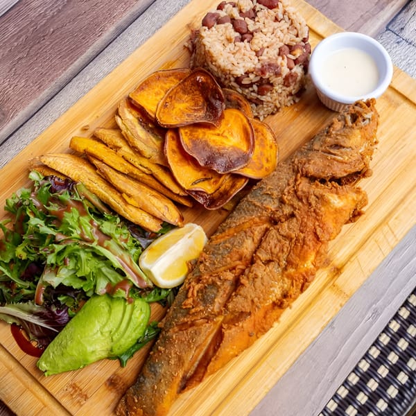 Fried whole fish with rice, beans, plantains, sweet potato chips, salad, avocado, and lemon.