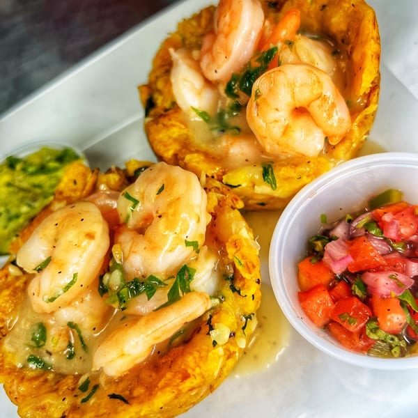 Two plantain cups filled with shrimp in sauce, served with guacamole and pico de gallo.