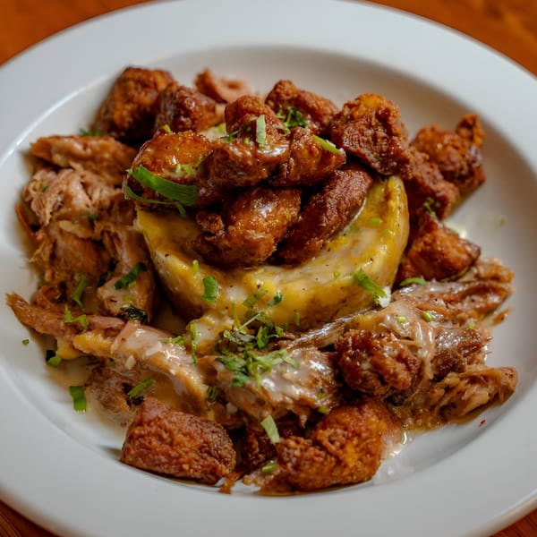 Latin-American dish with fried pork chunks, shredded meat, and mashed plantains on a white plate.
