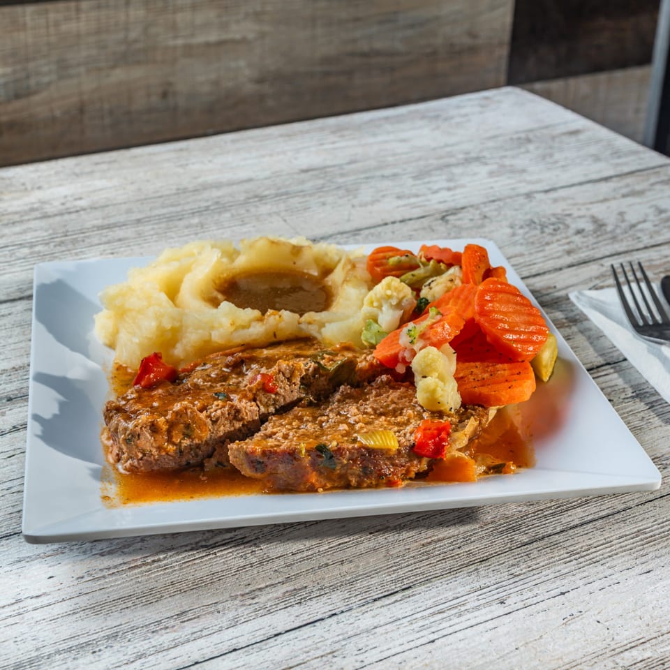 Meatloaf with gravy, mashed potatoes, and mixed vegetables on a white plate.