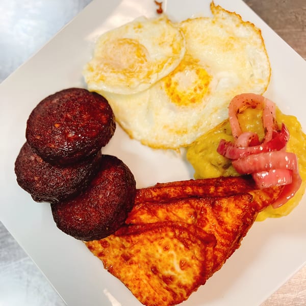 A Latin-American breakfast plate with fried eggs, chorizo, fried cheese, mashed plantains, and pickled onions.