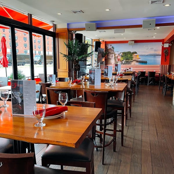 Interior of Sangria Cafe with wooden tables, black chairs, and a mural of a coastal town.
