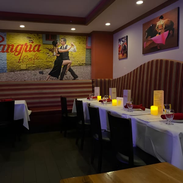 Dining room at Sangria Cafe with set tables, a large mural of tango dancers, and bullfighting art.