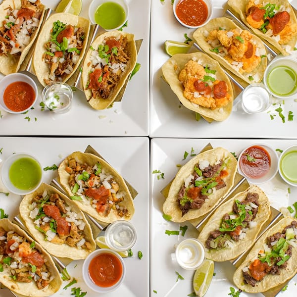 Four plates of Sangria Cafe tacos with various fillings, salsas, and lime wedges.