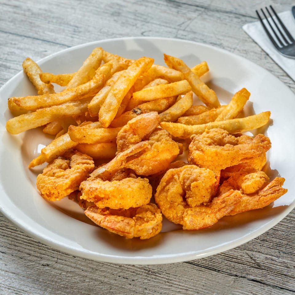A white plate filled with golden-brown fried shrimp and french fries on a wooden table.