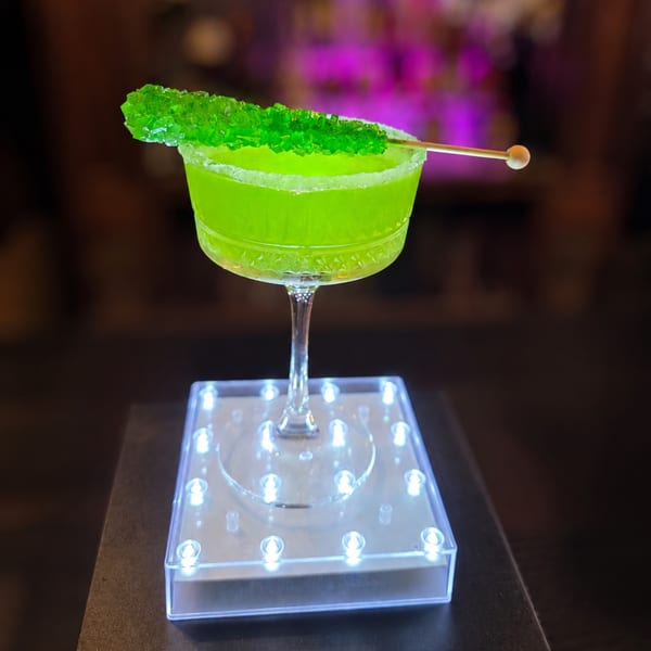 Bright green cocktail with a sugar rim and green rock candy stick on a light-up base.