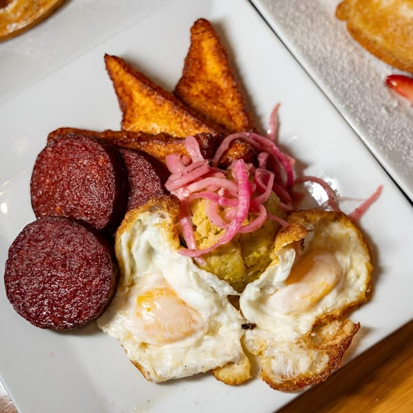 A Latin-American breakfast plate with fried eggs, salami, plantains, and pickled red onions.